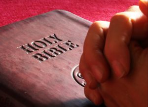 folded hands on Bible